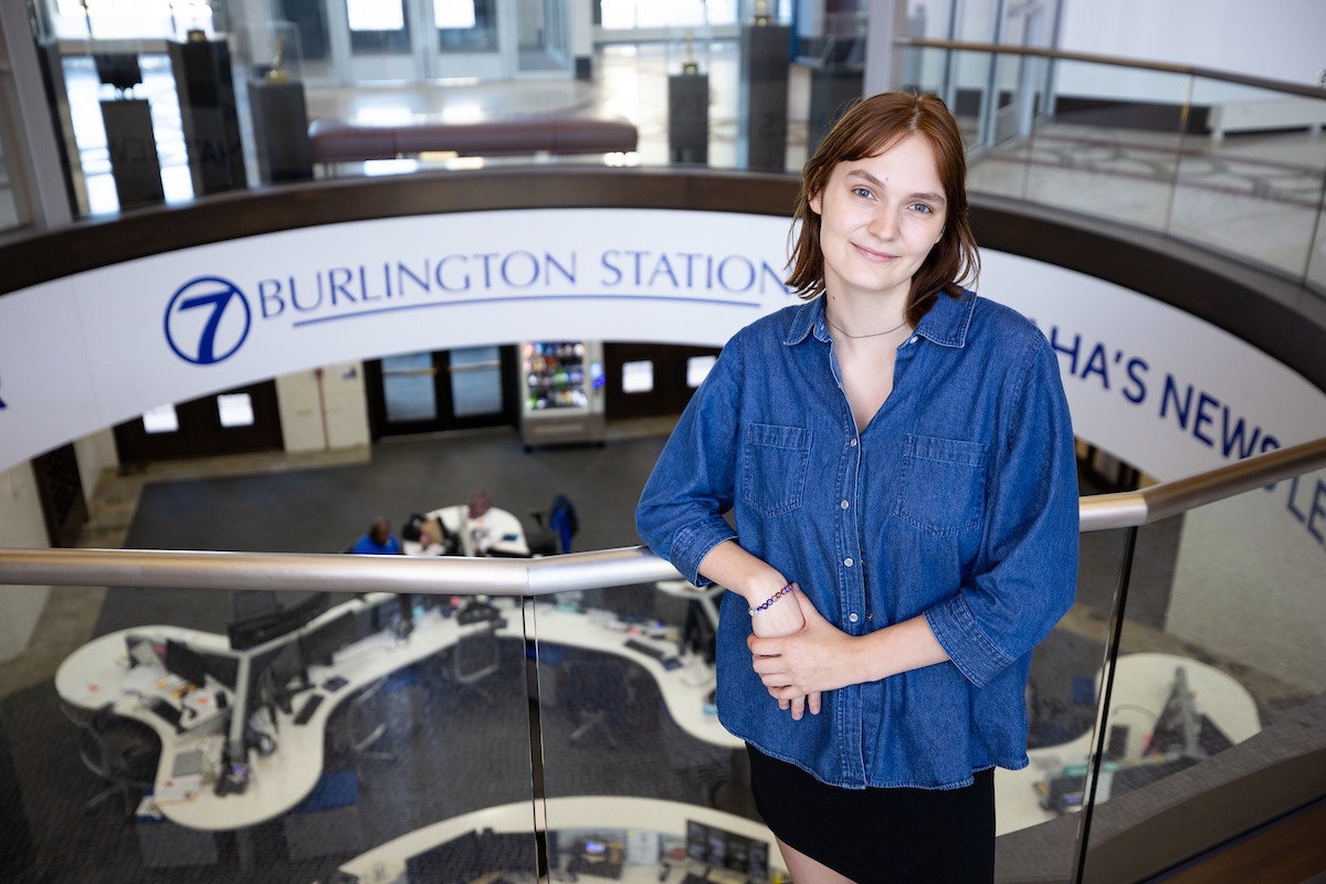 Jenna Janssen stands at a railing in front of the KETV 7 Burlington Station logo. 