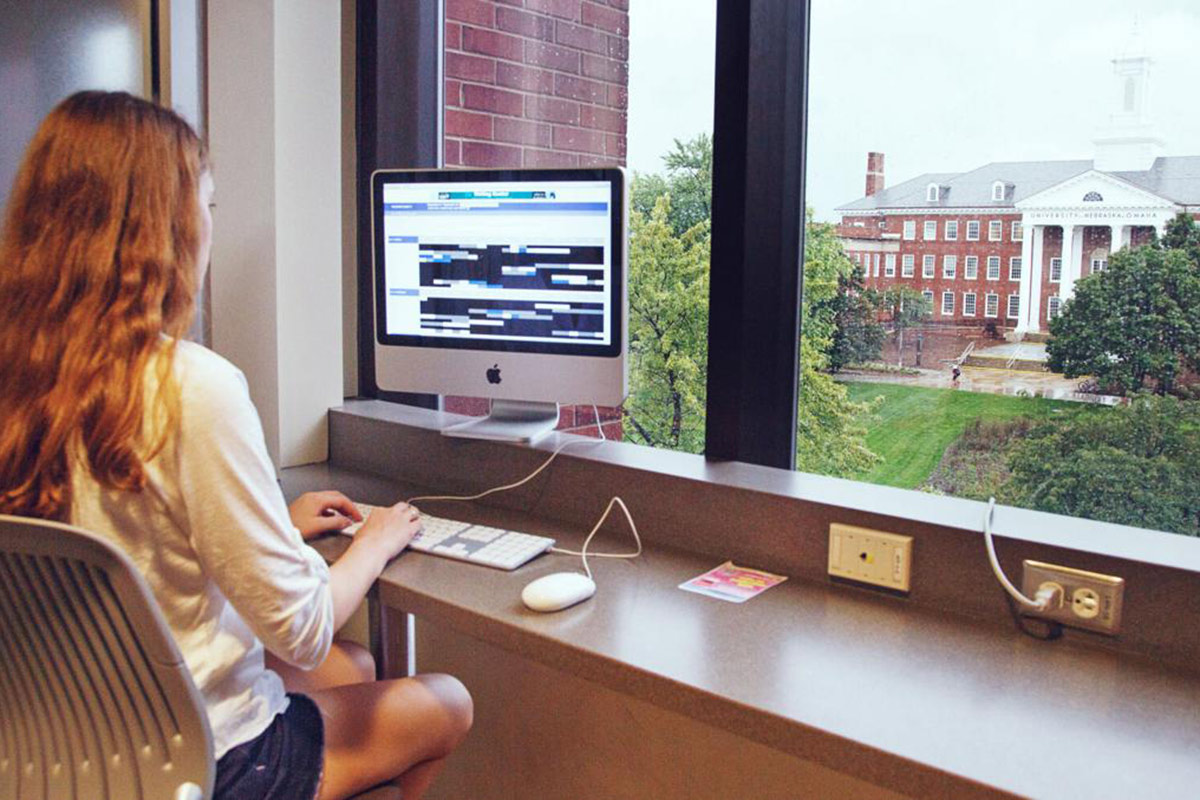Student working on computer in Roskens Hall, with the Arts and Sciences Hall in the distance