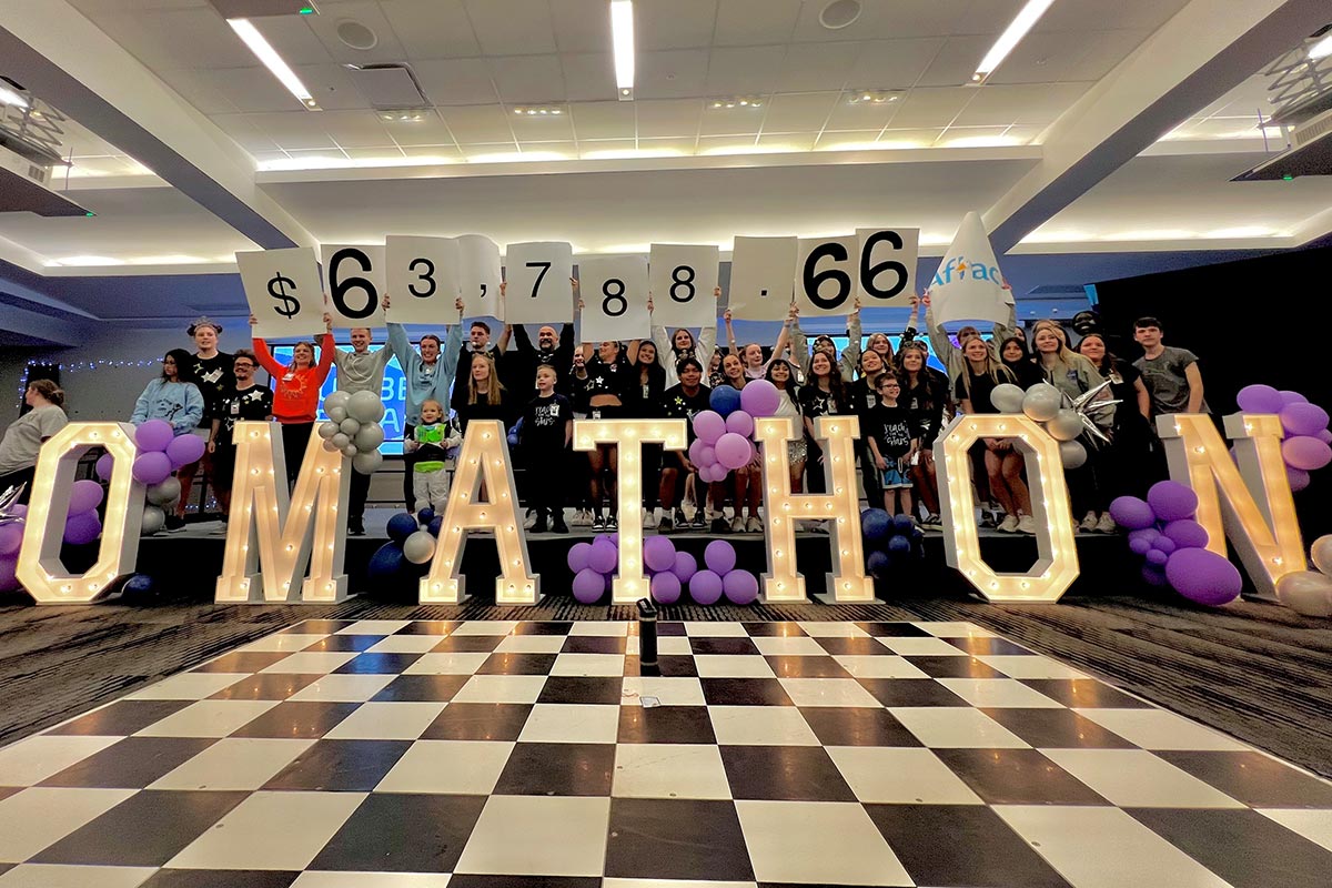 UNO Dance Marathon participants hold up placards announcing the final total