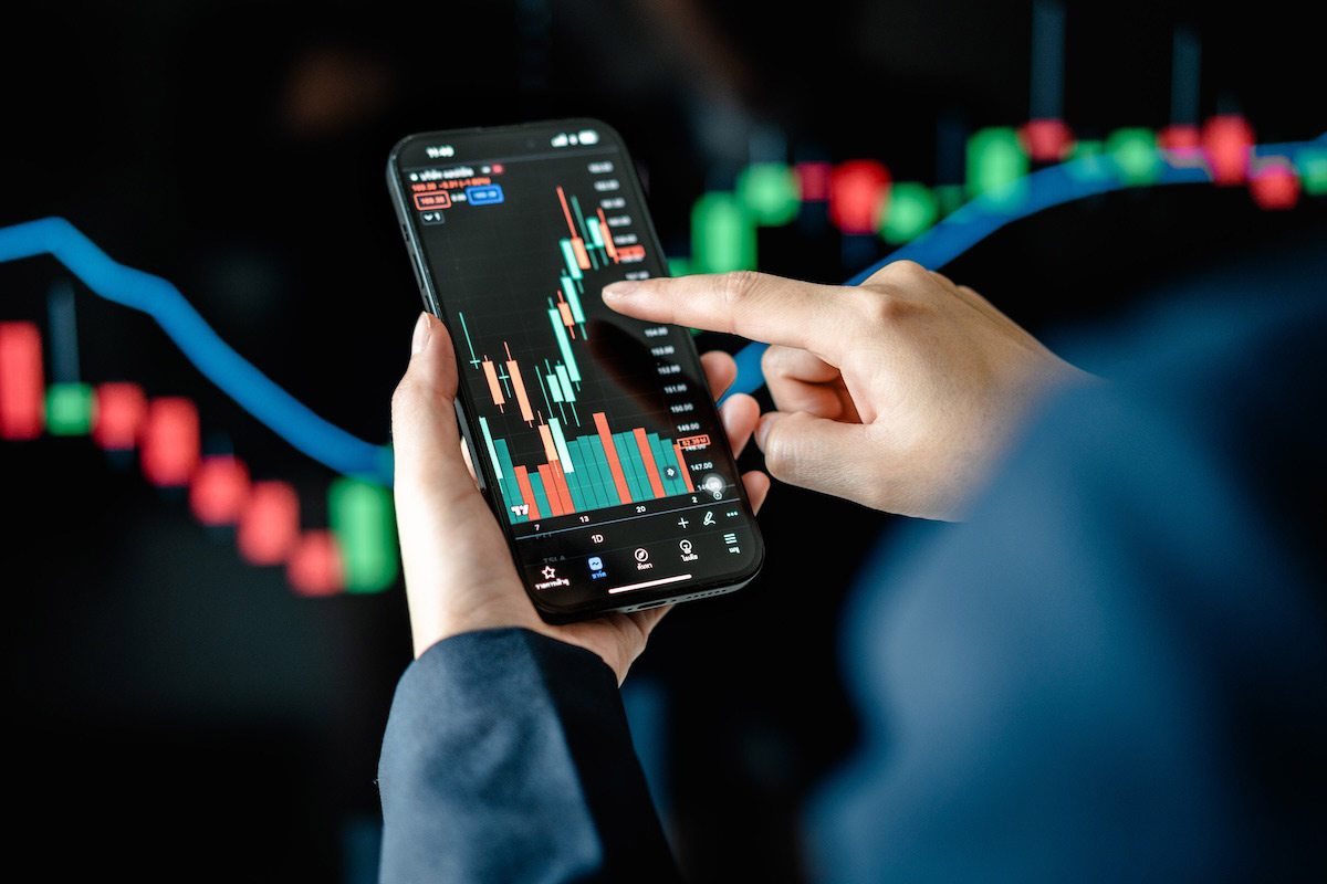 A person is analyzing stock market data on their smartphone, with a close-up view of a financial chart displaying red and green candlesticks and trend lines.