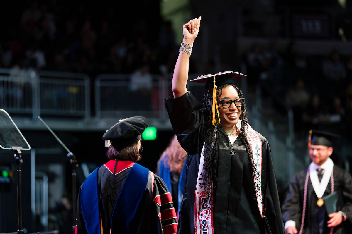 After receiving her diploma, the new alum celebrates with a hand in the air.