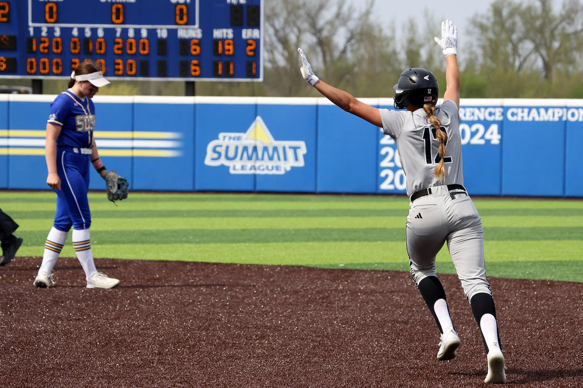 An Omaha Softball player celebrates after a hit sails out of the field for a run.