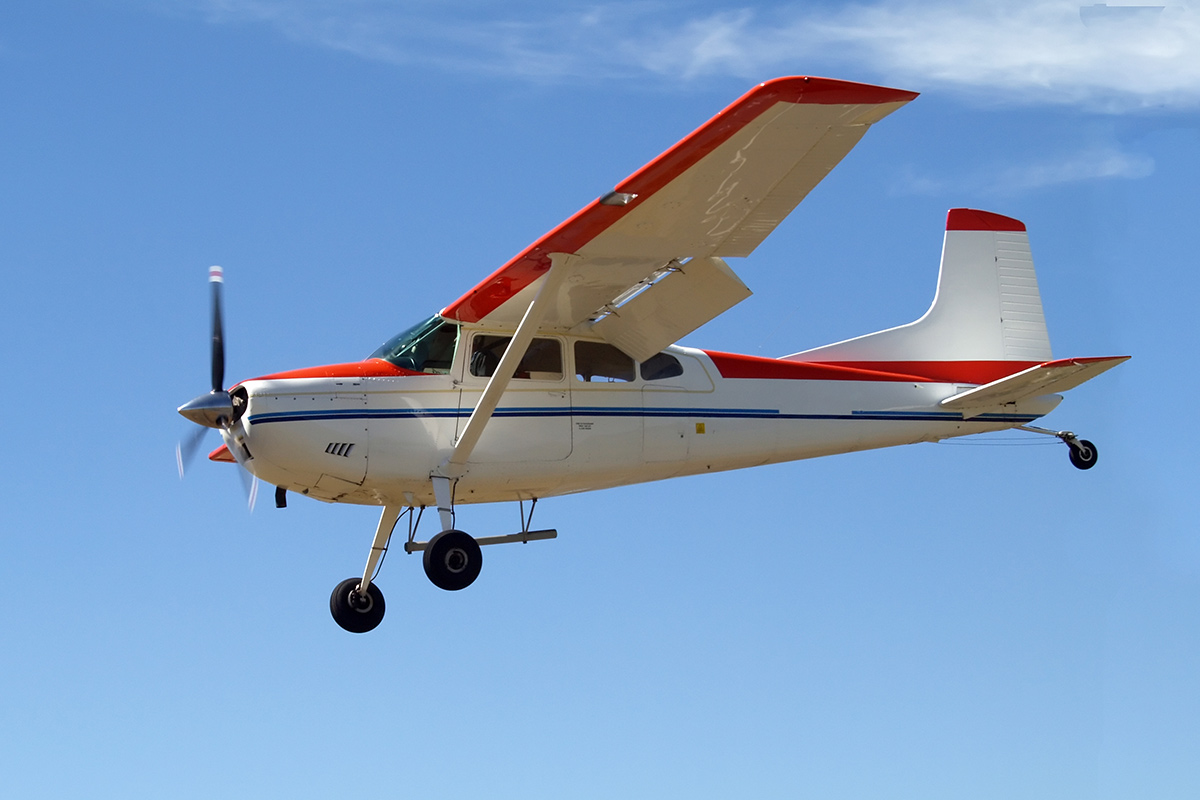 A generic Cessna 180 plane flies through blue skies.