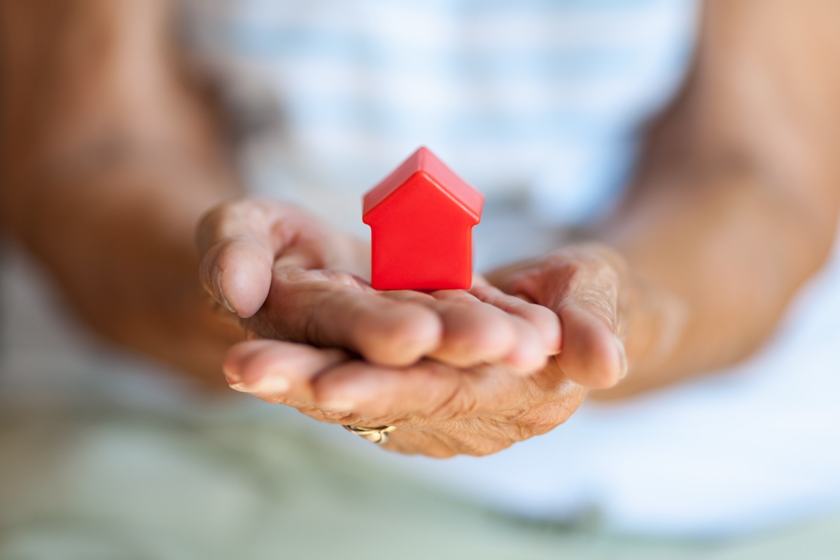 Elderly woman holding a small house in her hands.