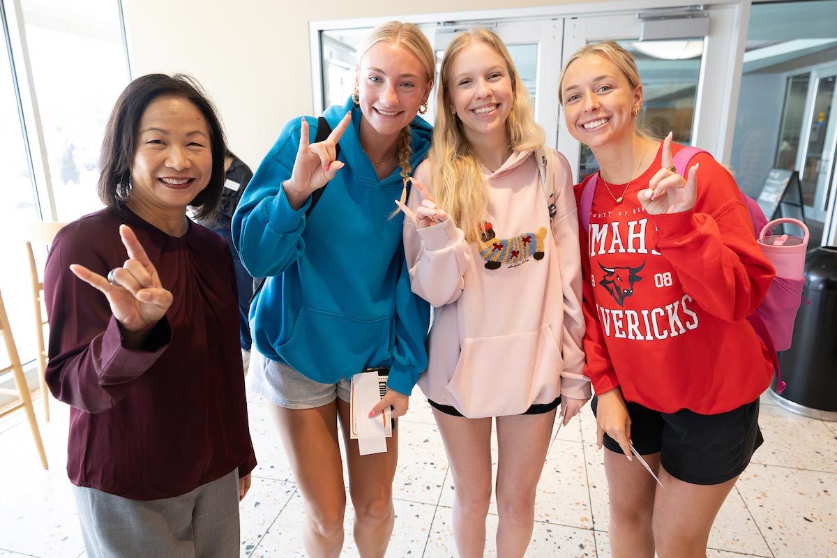 Chancellor Joanne Li poses with three UNO students, all smiling and throwing the Maverick “bull” hand sign during Coffee Talk with Spirit and Tradition. 