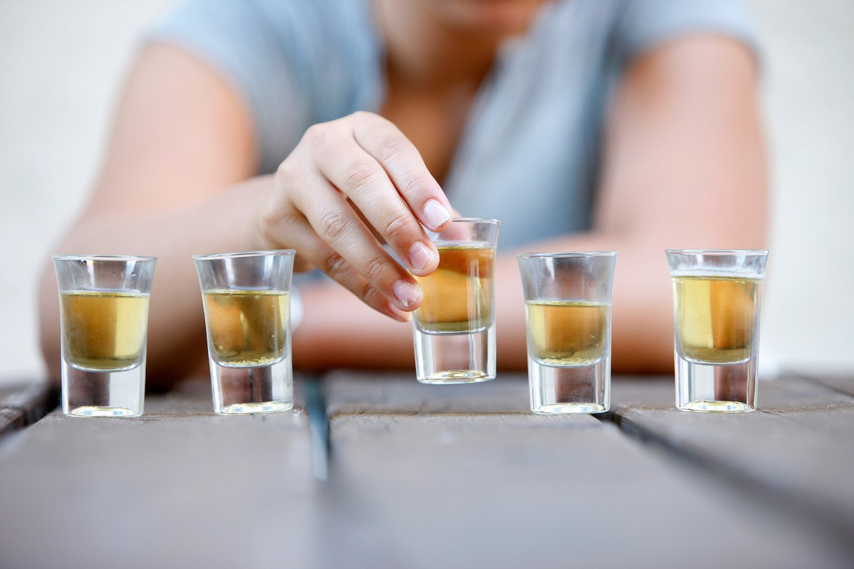 A photo of a person grabbing a full shot glass from a row of shot glasses. 