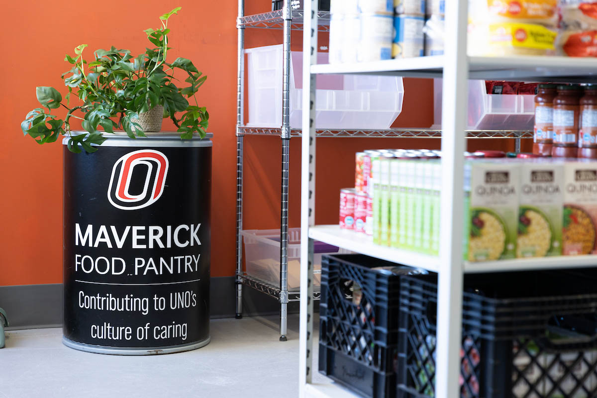 A black donation bin with the UNO logo stands beside metal shelving filled with pantry supplies. 