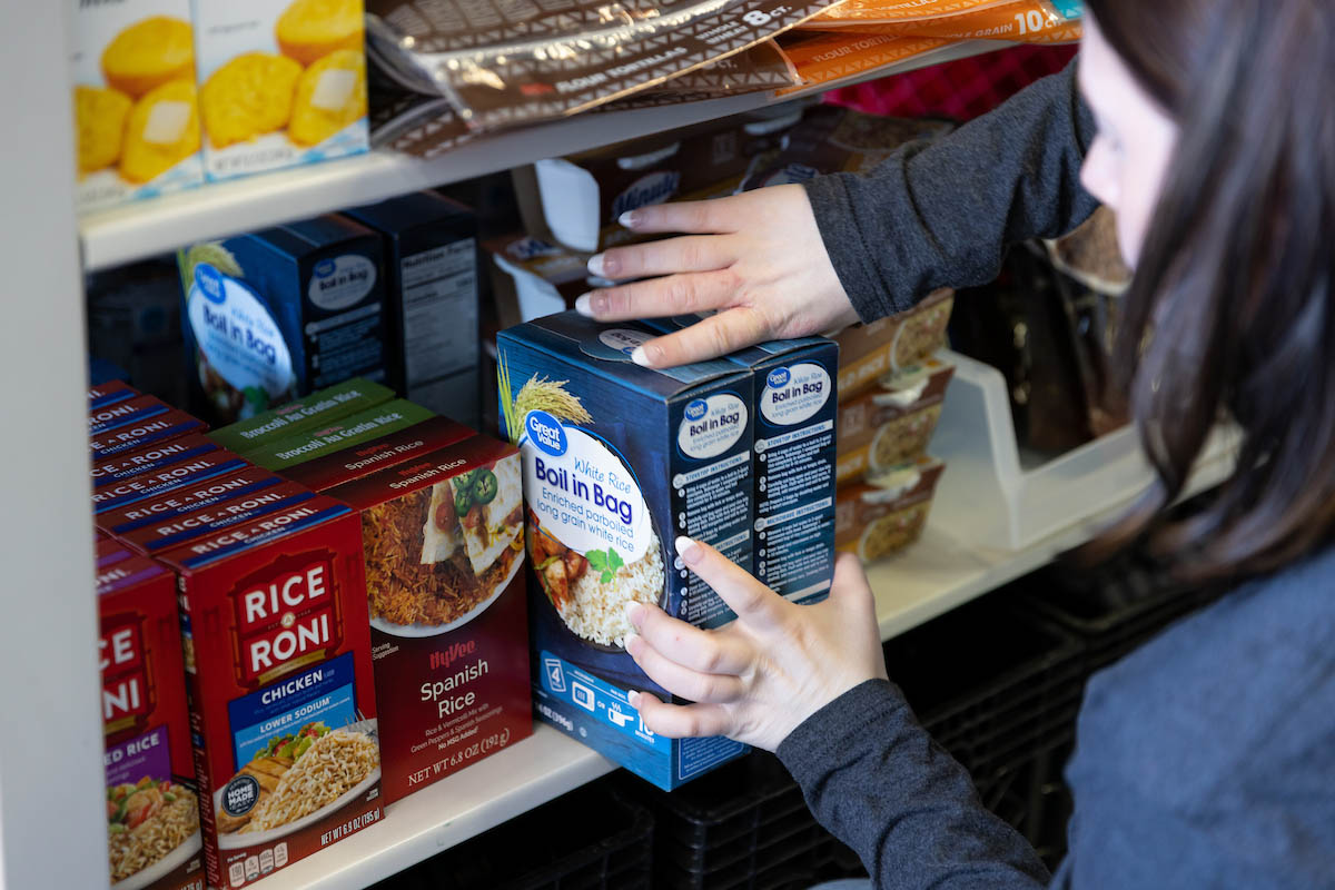 A woman places a box of rice on a lower shelf among other boxed pantry foods. 