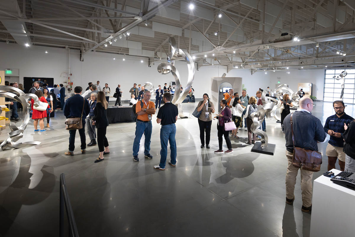 Attendees converse and explore exhibits in a large gallery space with abstract sculptures.