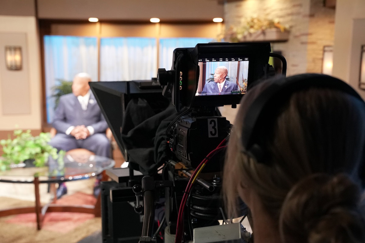 A camera operator films Mayor John W. Ewing, Jr. during a taping of Consider This at UNO’s television studio. The mayor is visible both in the studio and on the camera monitor. 