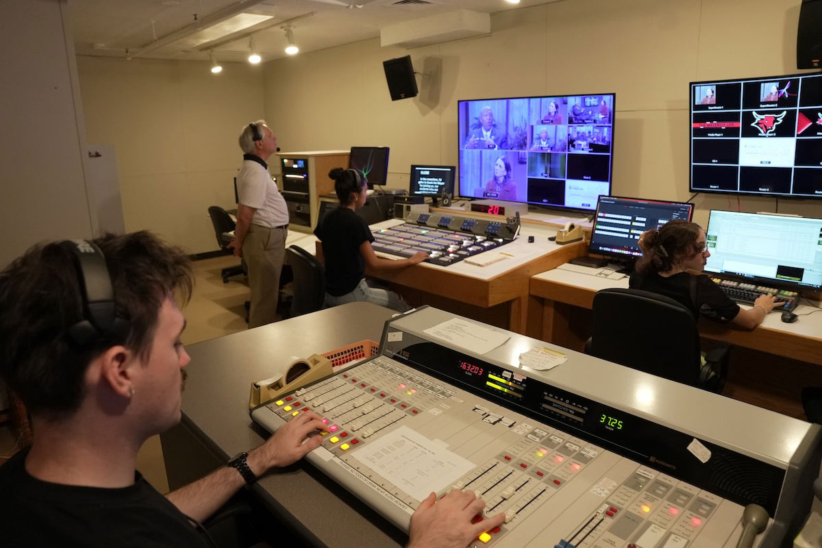 A group of UNO students and a faculty member operate sound, lighting, and video equipment in the control room while producing an episode of Consider This. 