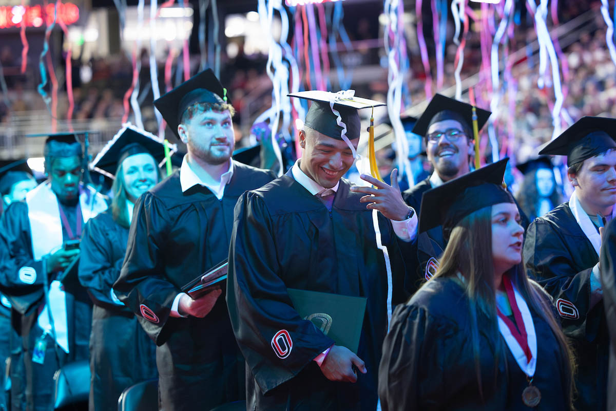 Graduates in caps and gowns celebrate as colorful streamers fall at the end of the commencement ceremony.