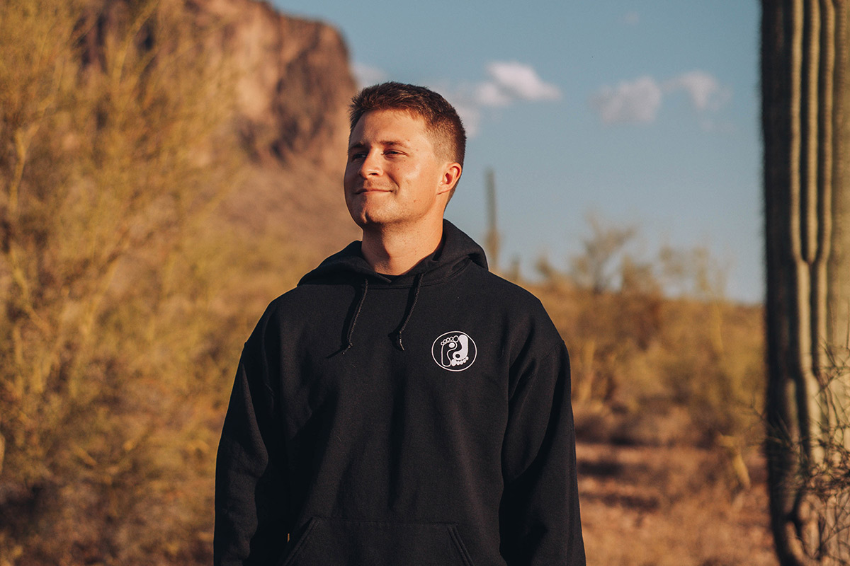 A figure stands in front of a desert vista of rock formations and a cactus.
