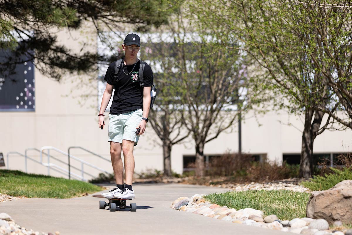 A student rides their skateboard near the MBSC Plaza and Allwine Hall.