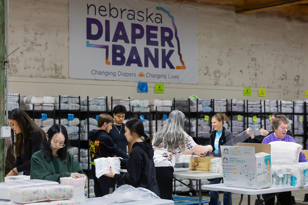 Students stand at assembly lines and organize diapers into packaging.  