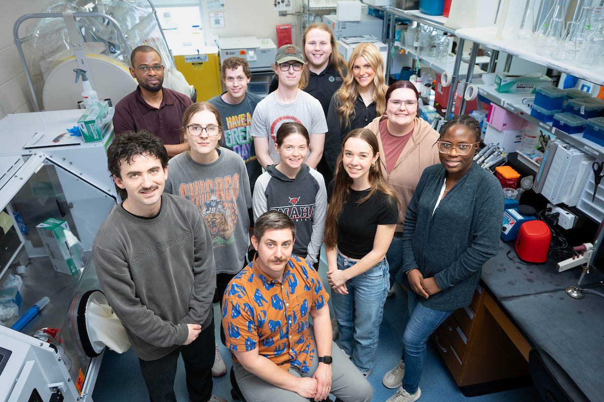 Group of researchers observing colleague working inside a lab enclosureGroup portrait of lab team standing together in laboratory