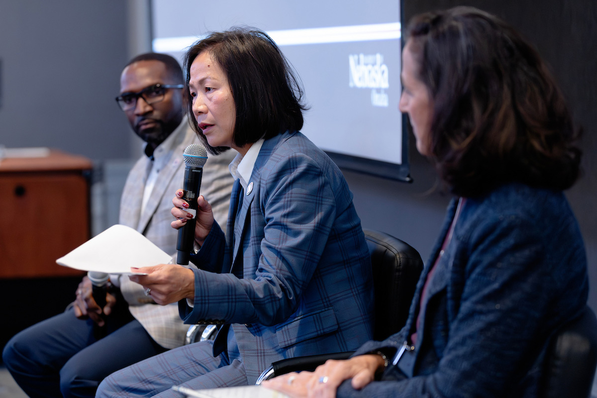Chancellor Li, seated between two people, holds notes while speaking into a microphone.