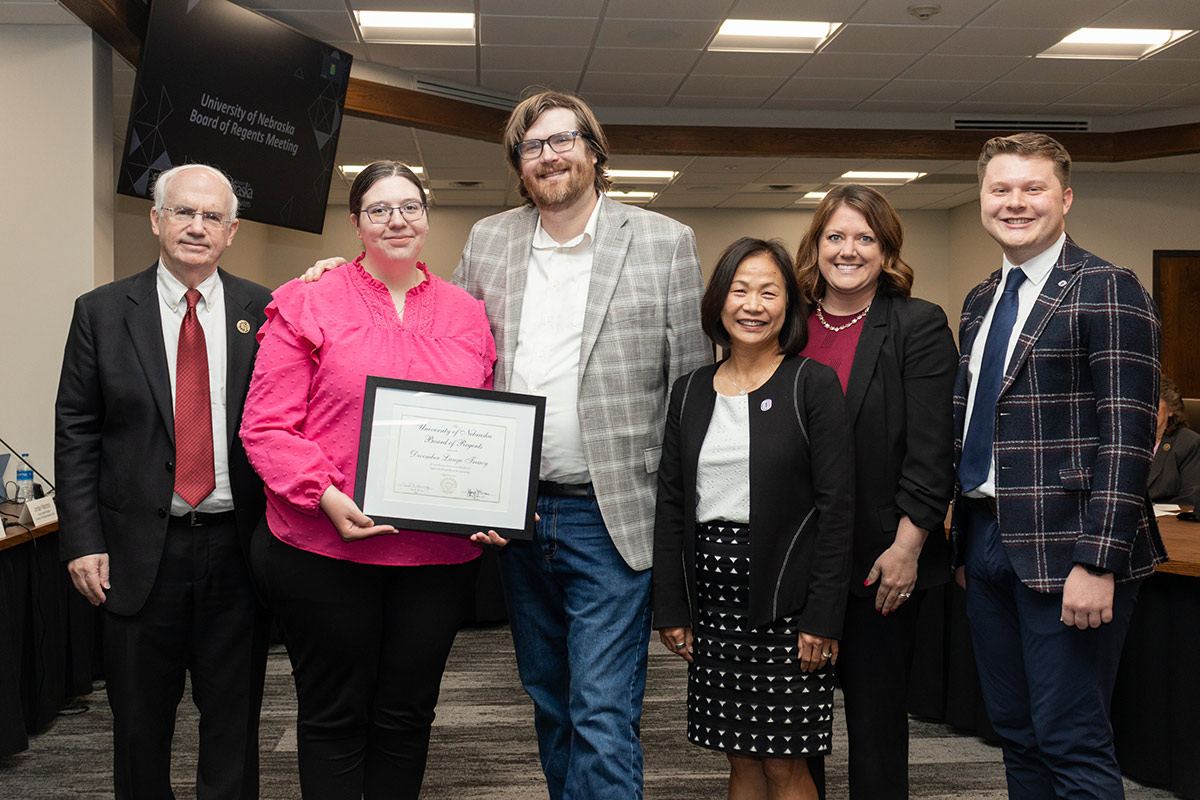 A woman poses with an award certificate, loved ones, and colleagues.
