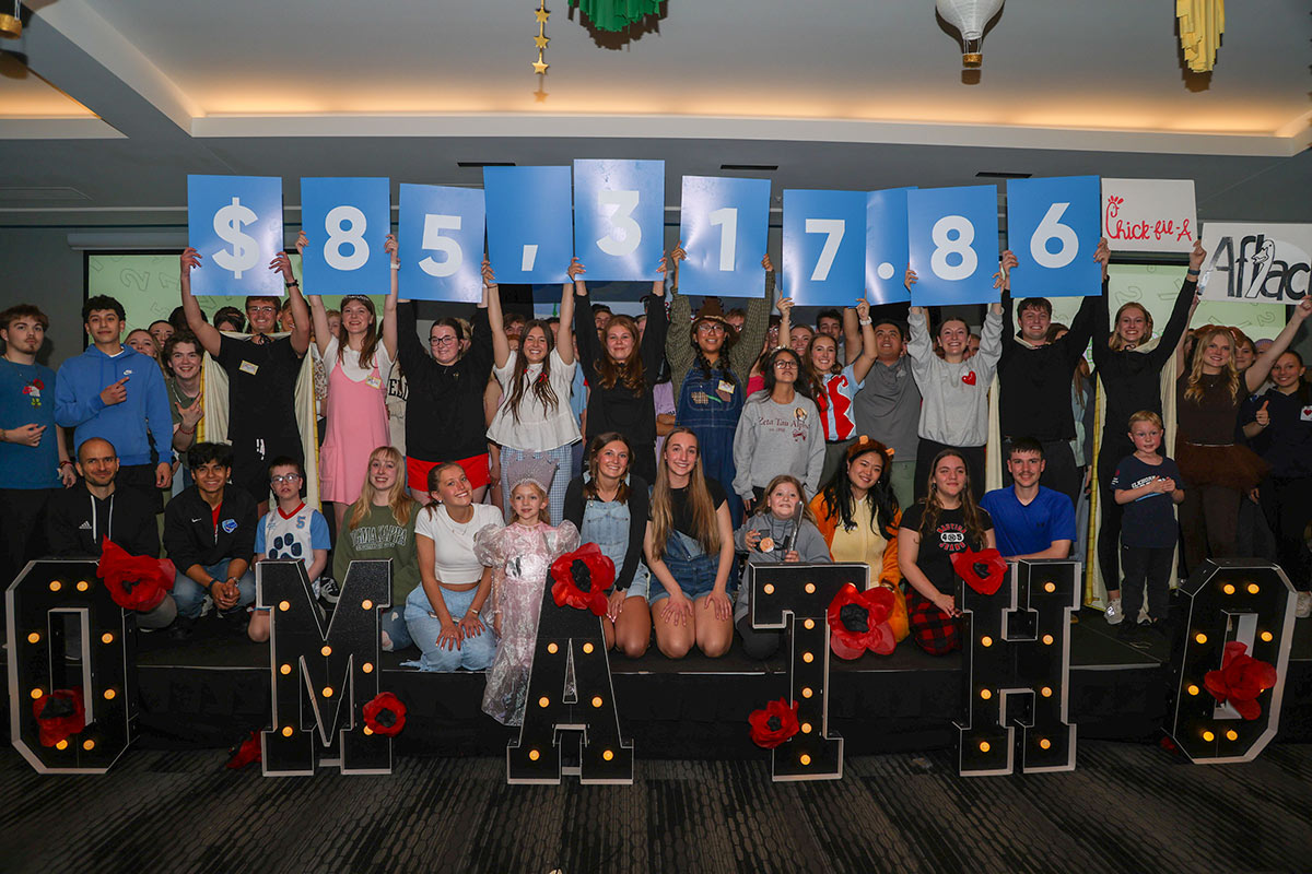 A group of UNO students pose in two lines, while the back row of students hold signs with numbers that show the event’s fundraising goal, while students in the front row kneel behind letters that read OMAthon.