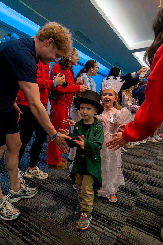 Two young Miracle Kids walk through a tunnel of UNO students giving high-fives. 