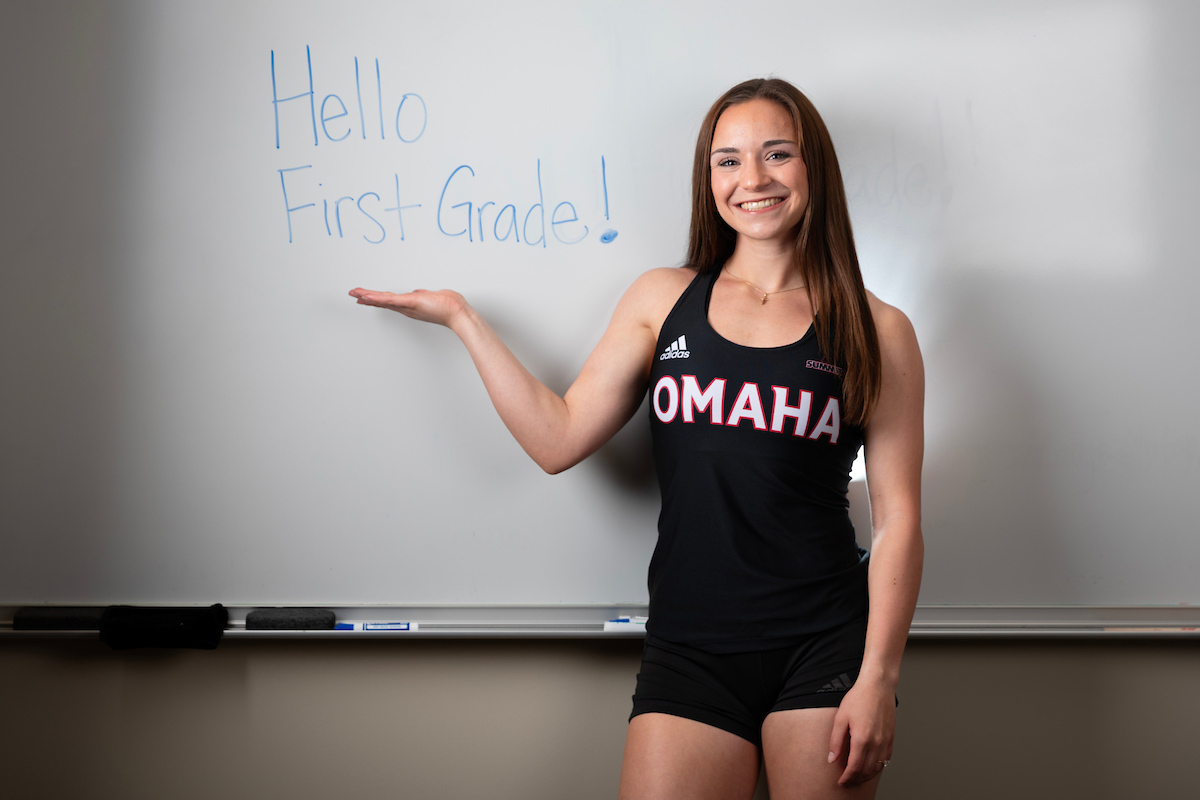 Emma Klein stands in front of a white board with “Hello First Grade!” written on it. 