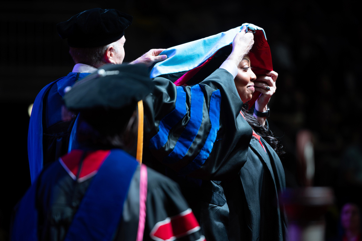 Faculty member places a doctoral hood over a graduate during a hooding ceremony.