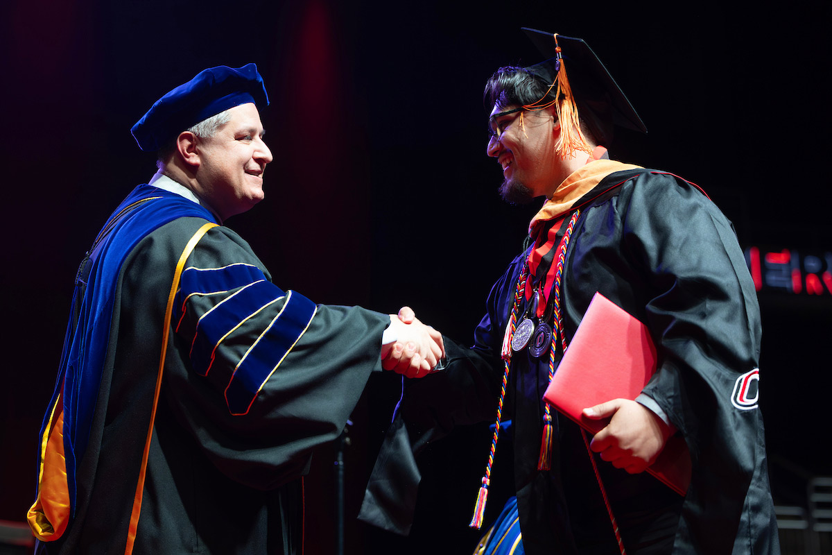 Graduate shakes hands with a faculty member while receiving a diploma on stage.
