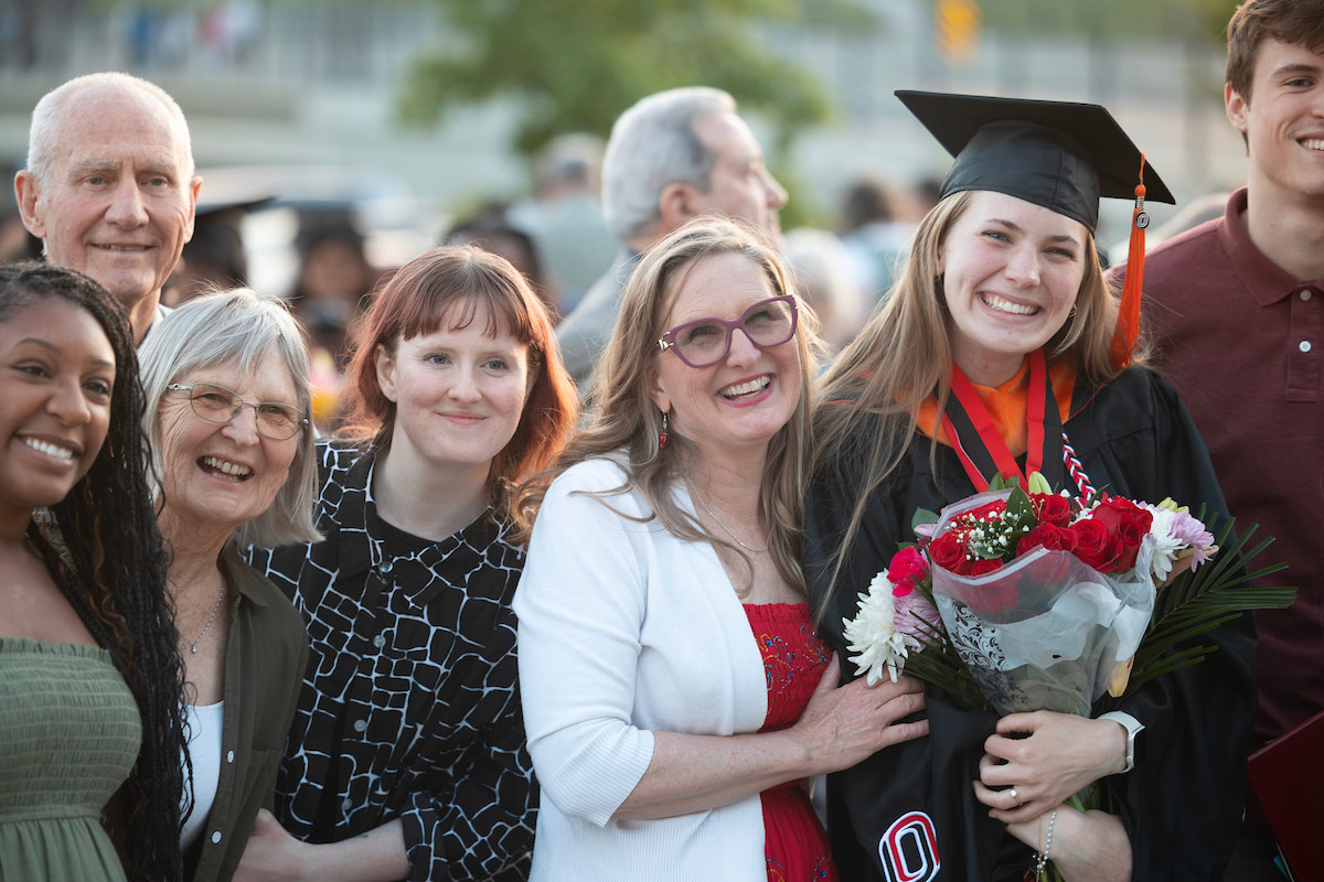 Graduate poses with family members while holding flowers after the ceremony.