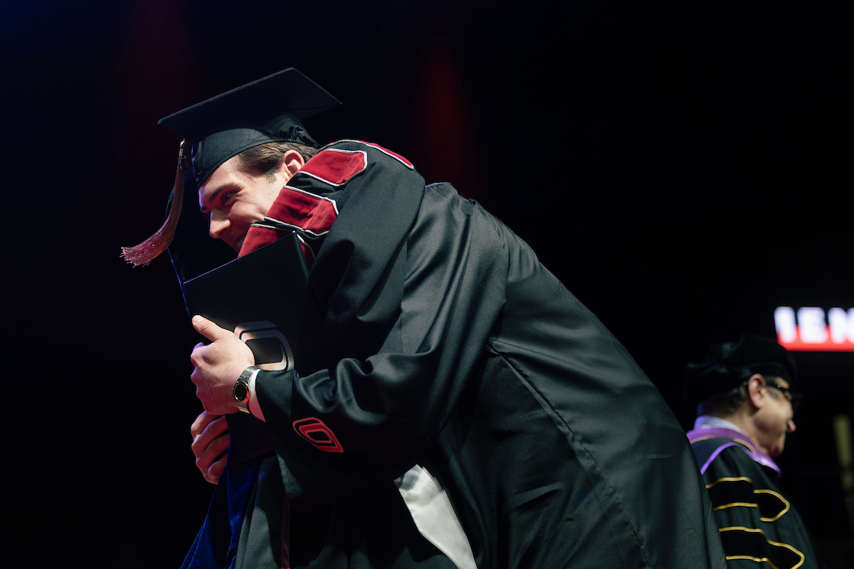 Graduate in cap and gown embraces Chancellor Li on stage during the commencement ceremony.