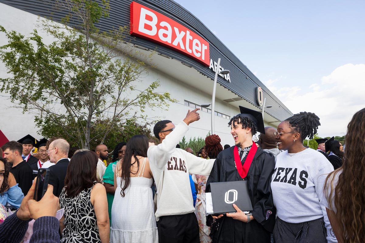 Graduate holding a diploma celebrates with friends and family outside Baxter Arena.
