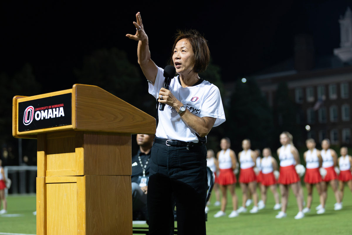 A woman at a podium with a microphone addresses a crowd.