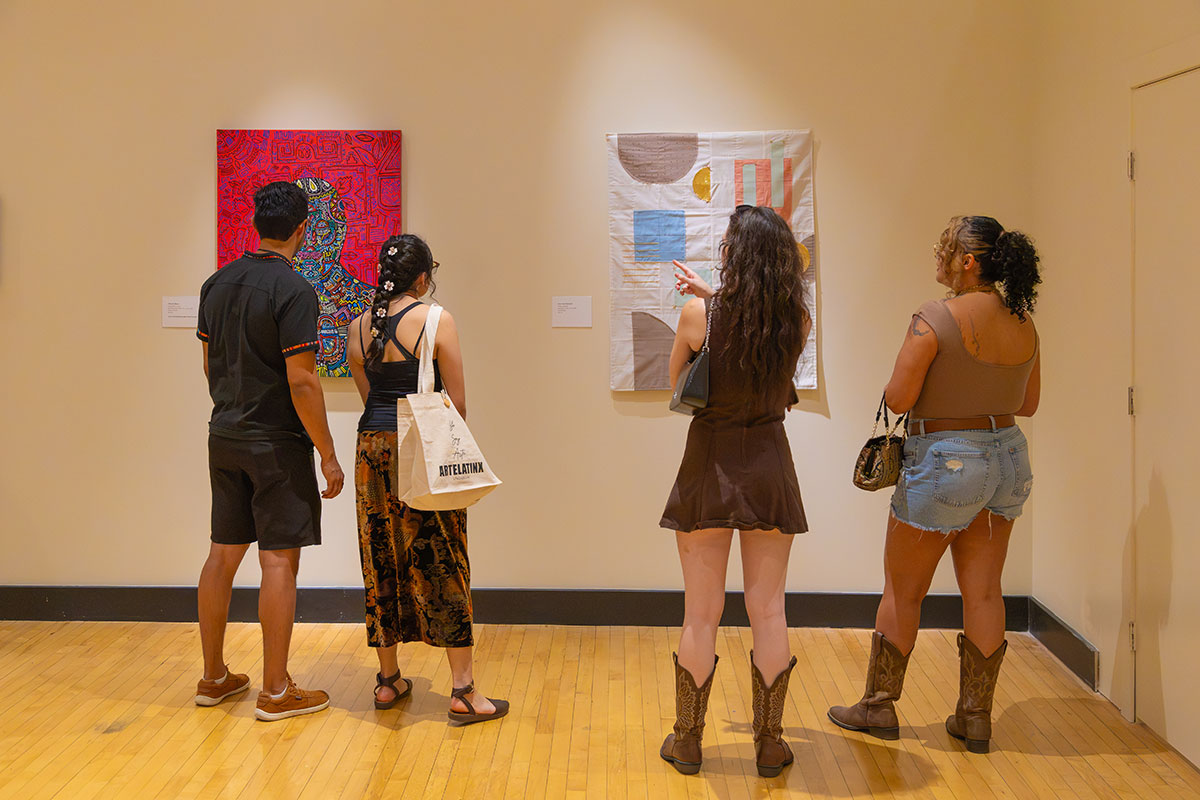 Four students are captured from behind as they view art on a wall in a gallery.