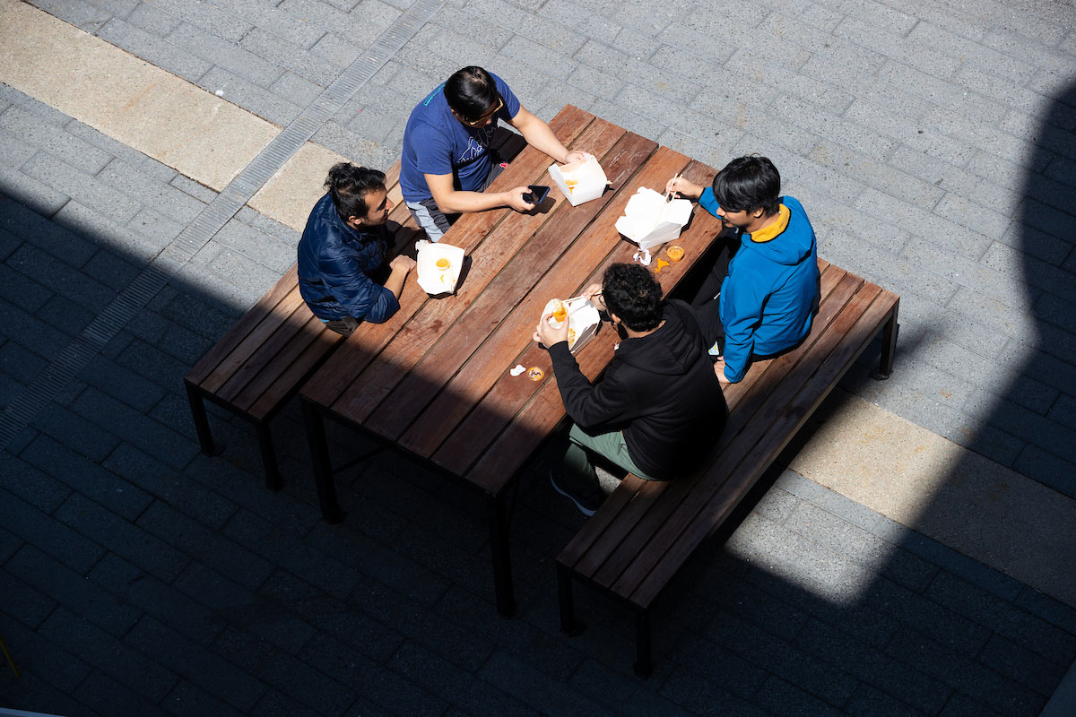 four young men sit together at a table, eating and talking.