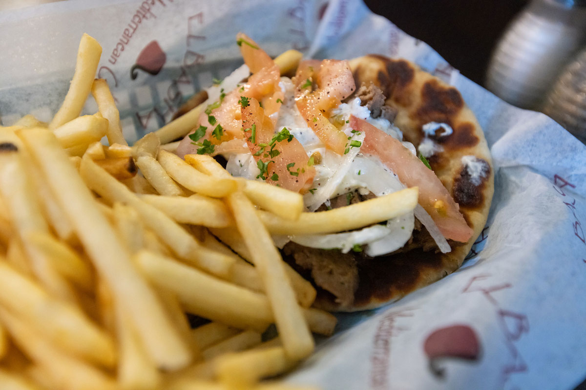 Pita bread with meat and veggies sits on a plate with french fries.