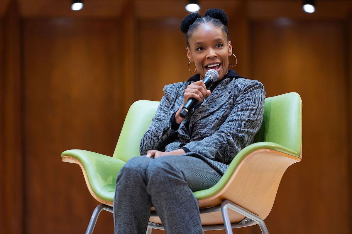 A woman holding a microphone sits in a green chair on a stage.