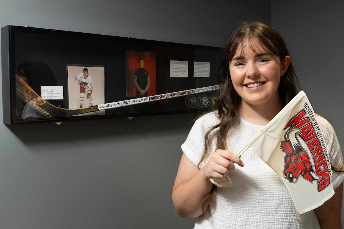 Uno grad student Emma Mitchell poses with UNO hockey memorabilia in the archives.