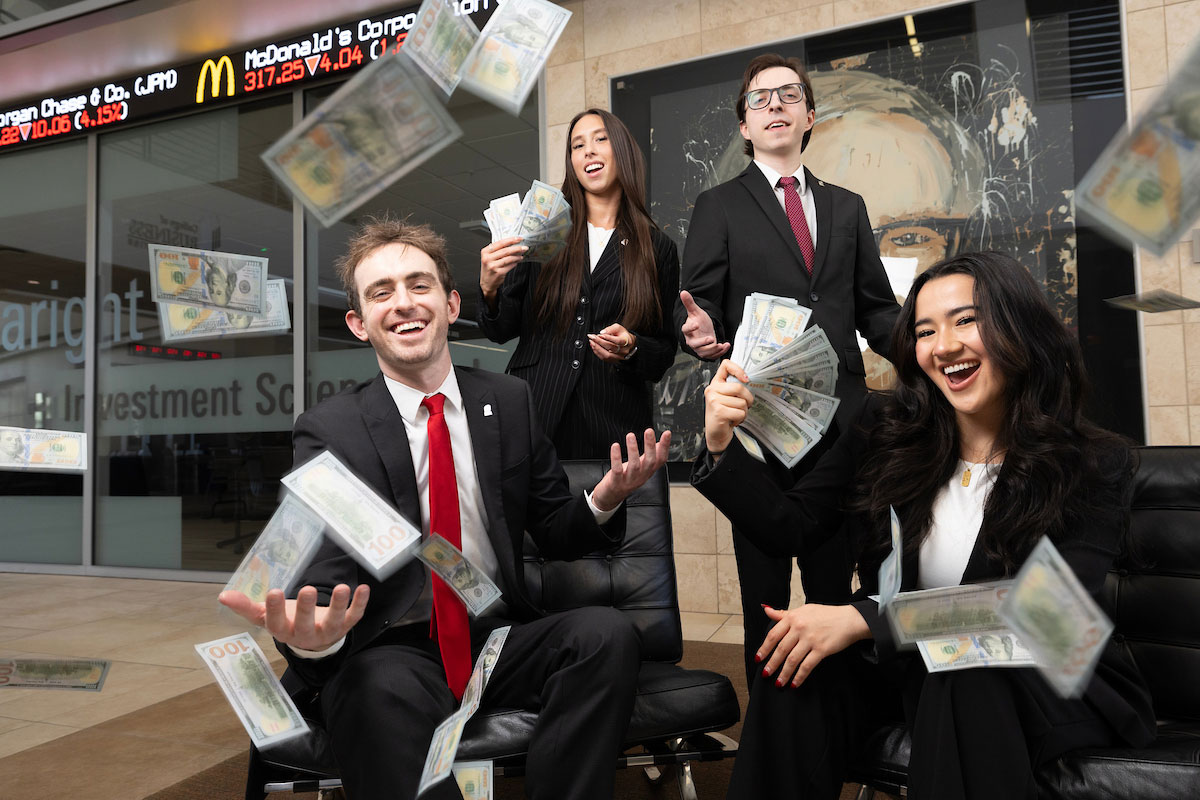 Students pose and throw money in front of the stock ticker in UNO's Mammel Hall.