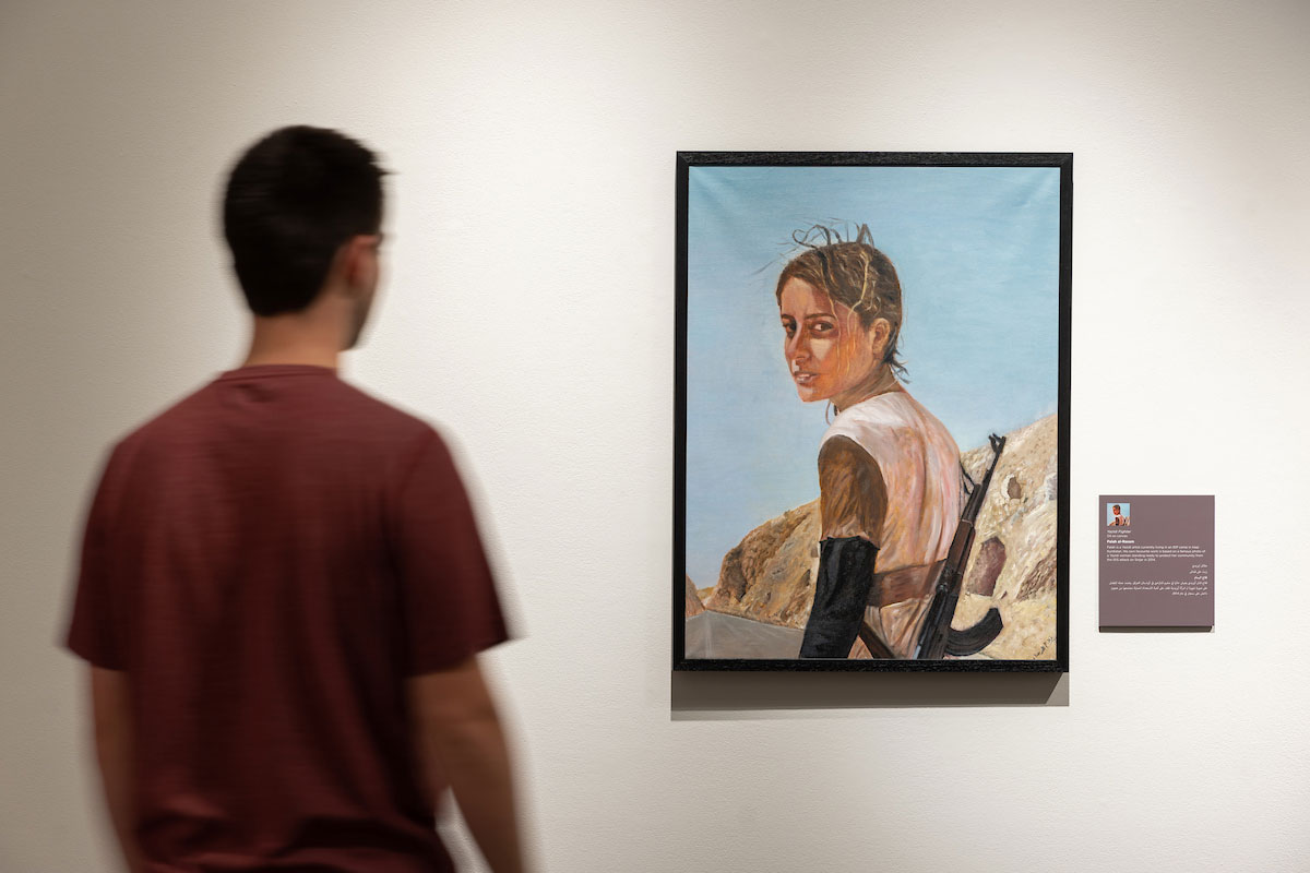 A student stands in front of a white wall with a painting on it in the UNO art gallery.