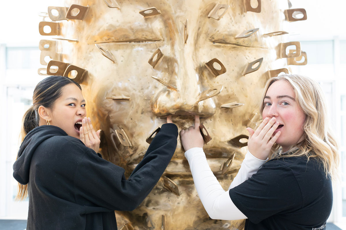 Students pose in front of the giant bronze head statue in Mammel Hall.