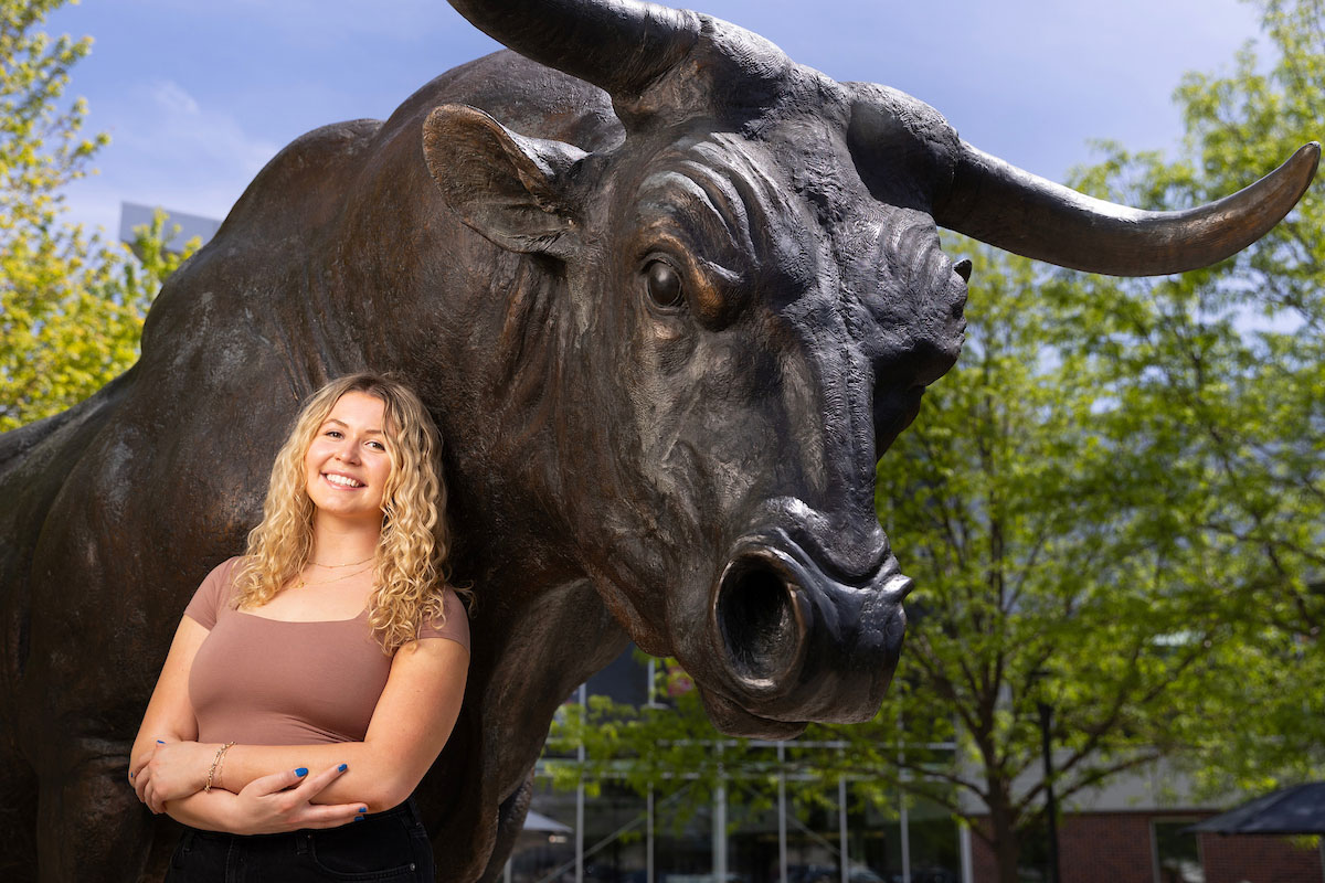 A student poses in front of the Maverick monument