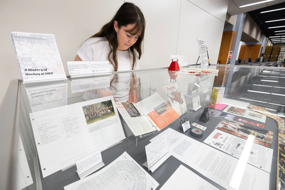 A woman stands behind a glass display case, adjusting the items inside.