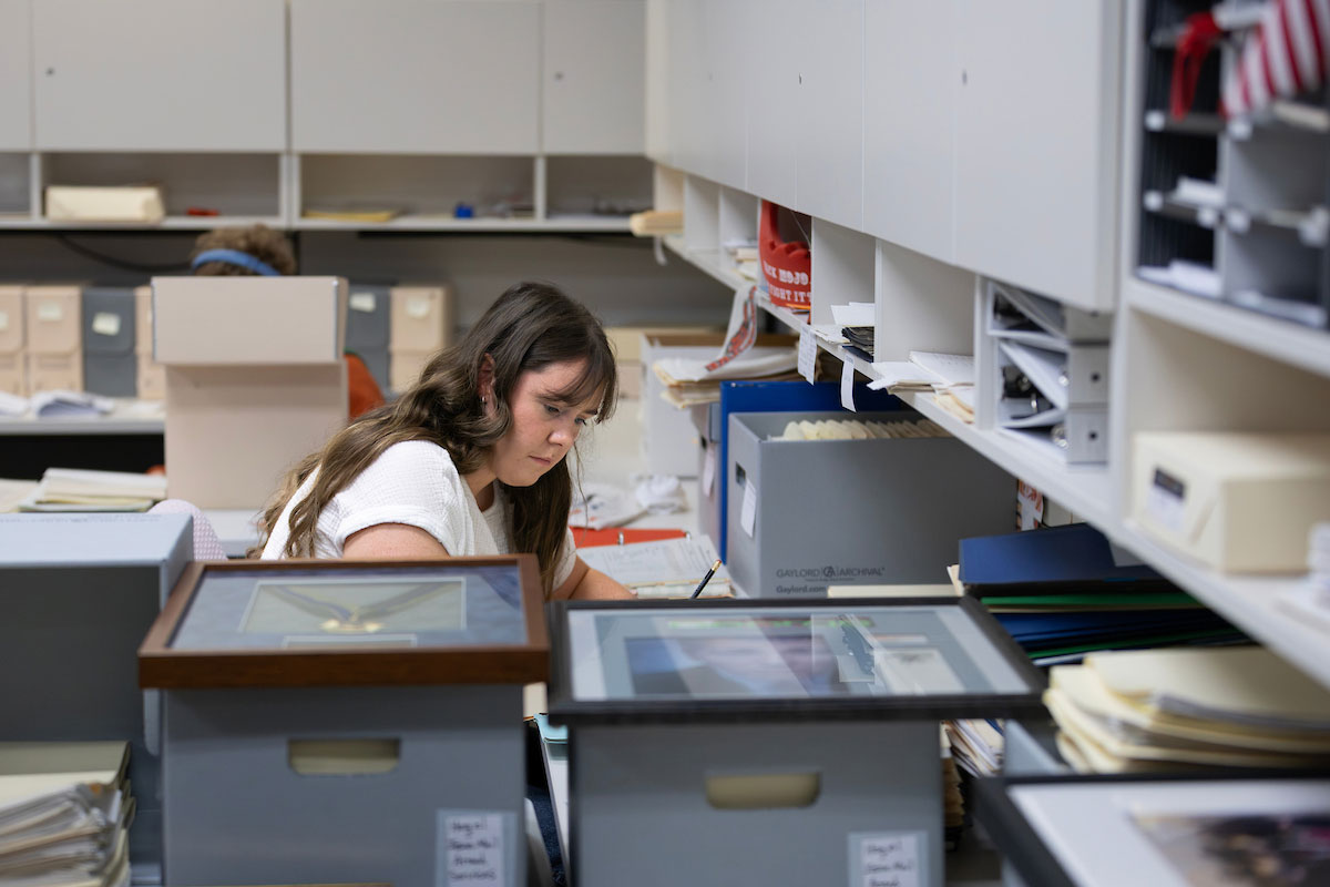A woman sits at a desk, surrounded by materials in her office.