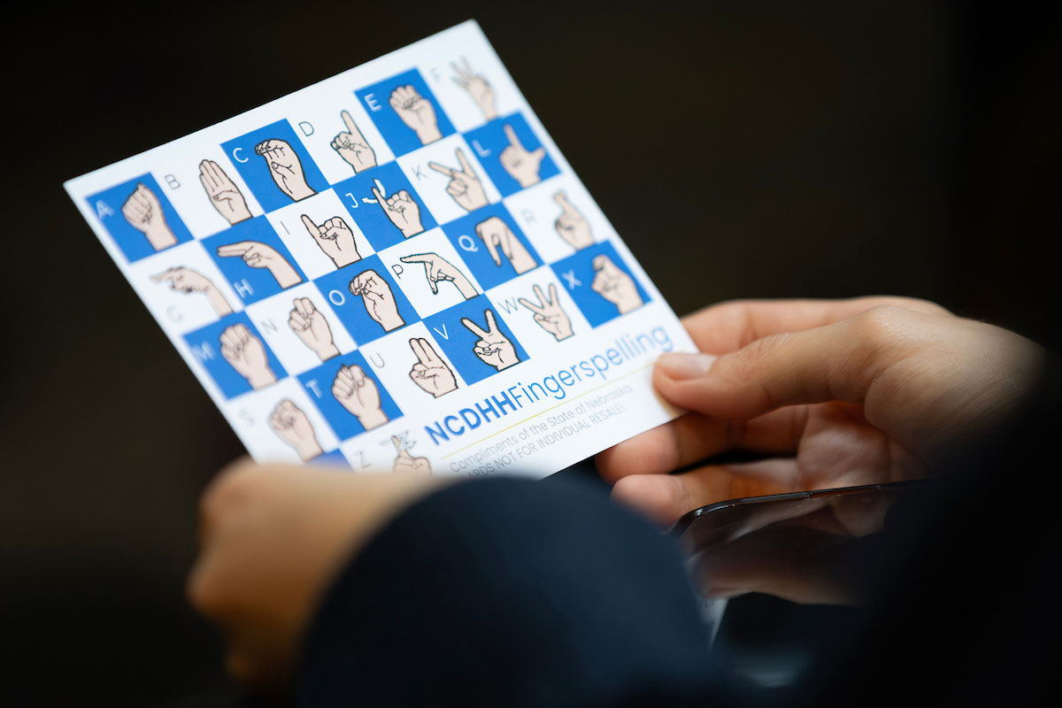 A student holds a sheet with some ASL words.  