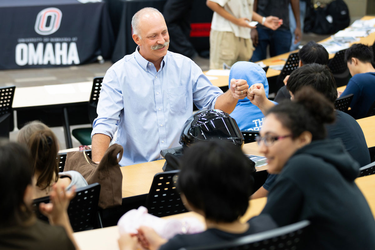 A man in a lecture hall fist bumps a student.
