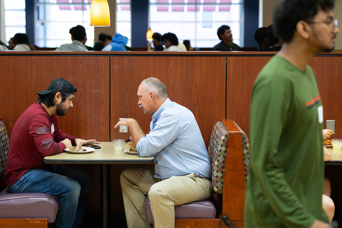 Two men sit in a booth in a food hall talking intensely.