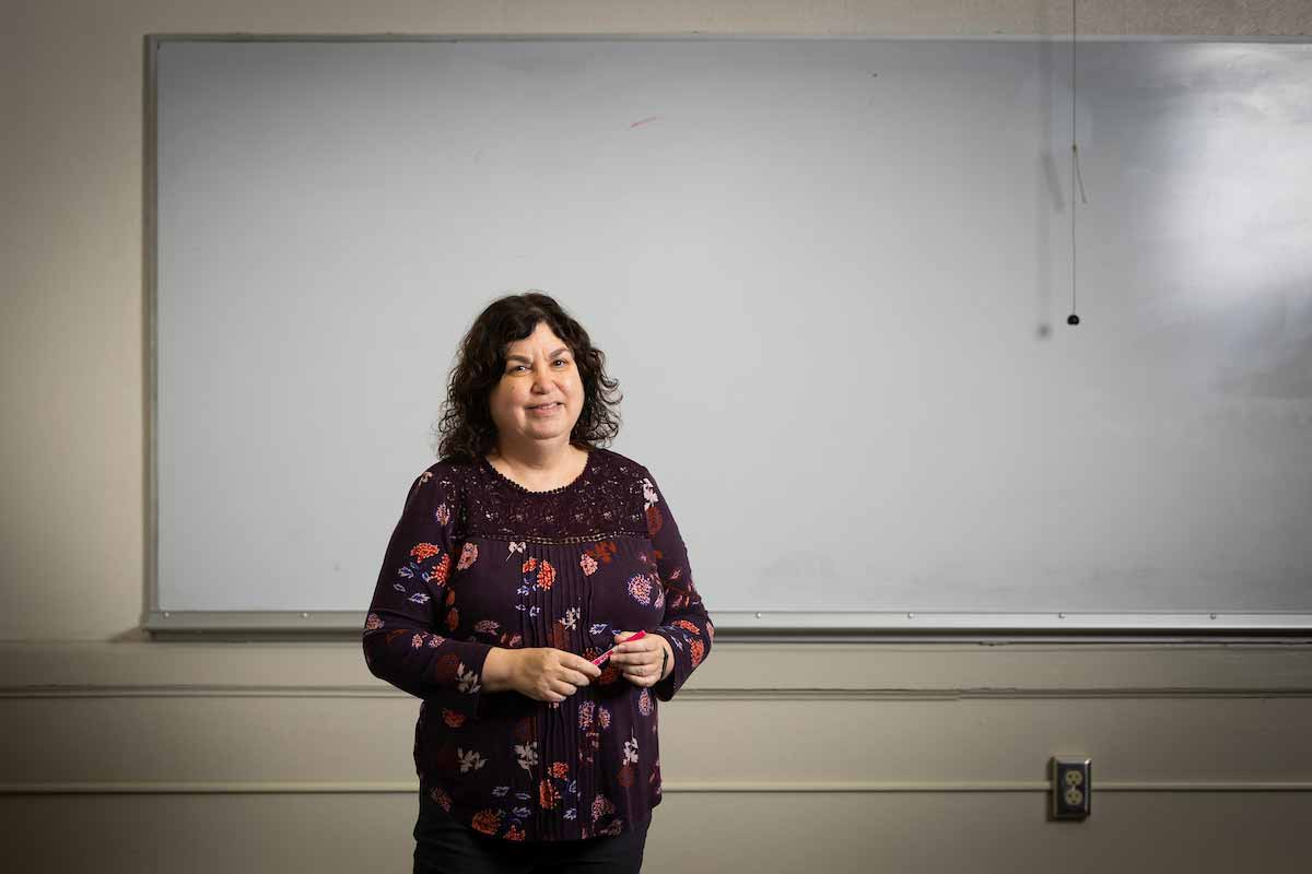 Roni Reiter-Palmon poses in front of a classroom marker board.  
