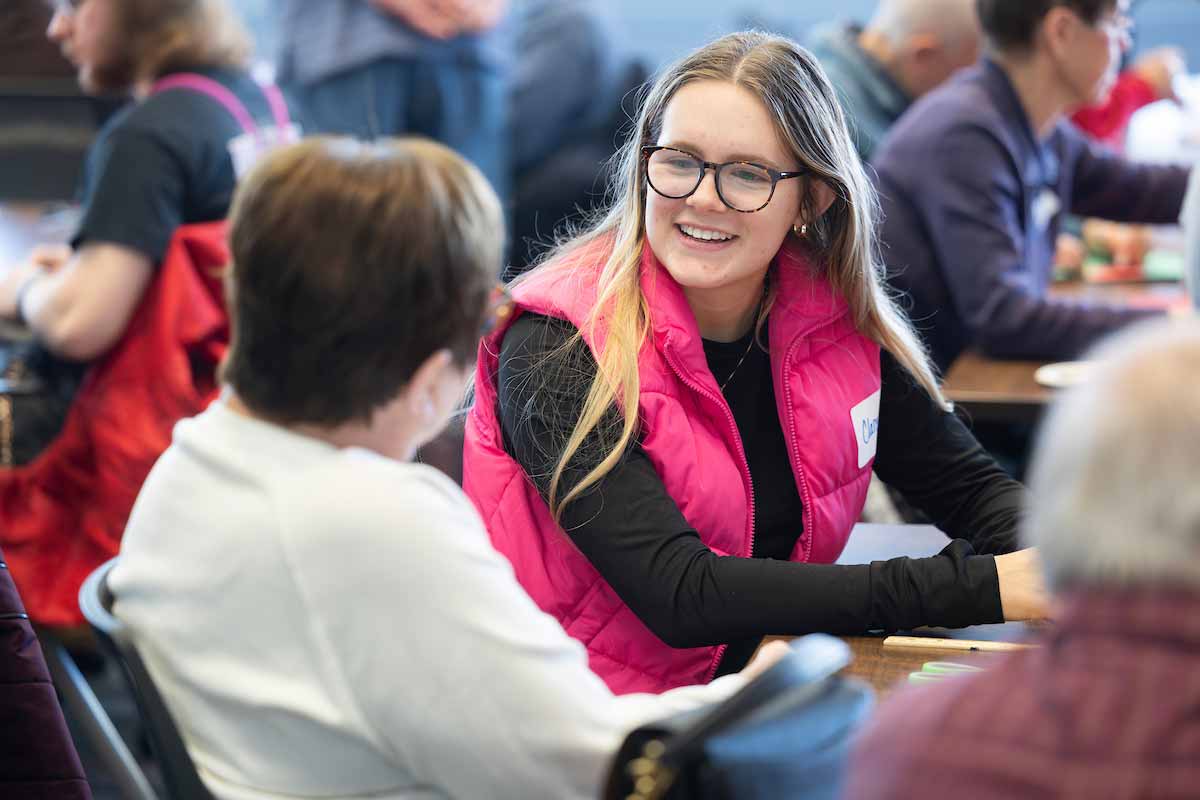 A student smiles while speaking to an elder adult at a table 