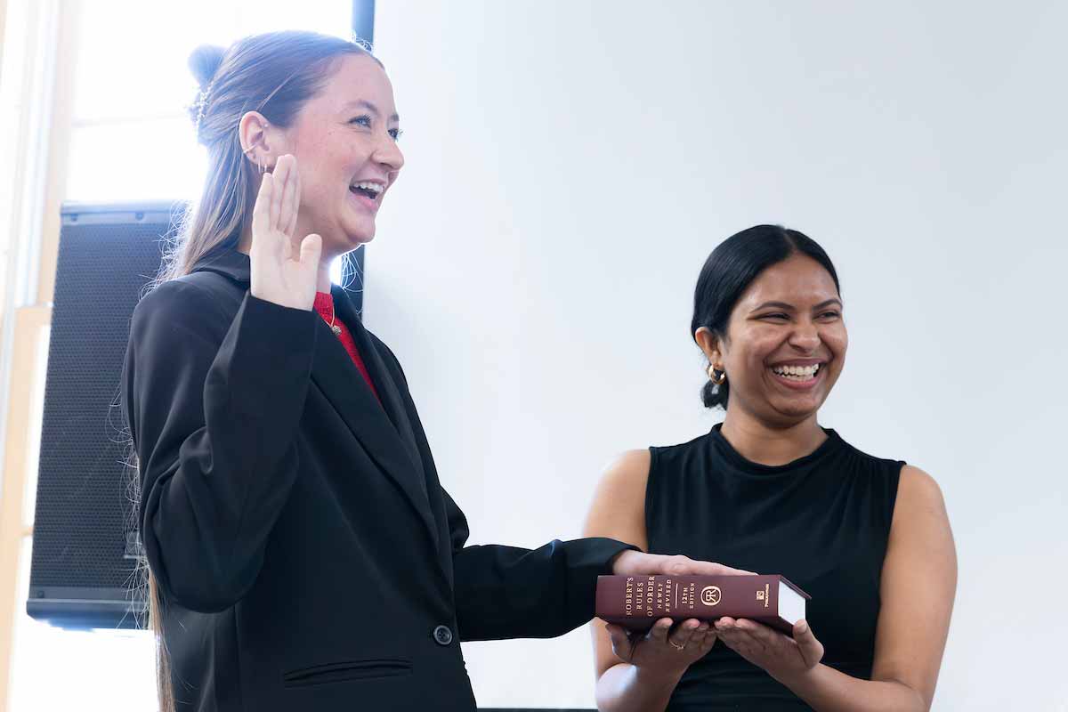 A woman places her left hand on a Robert’s Rules of Order book held by another woman, while raising her right hand in the air to take an oath. 