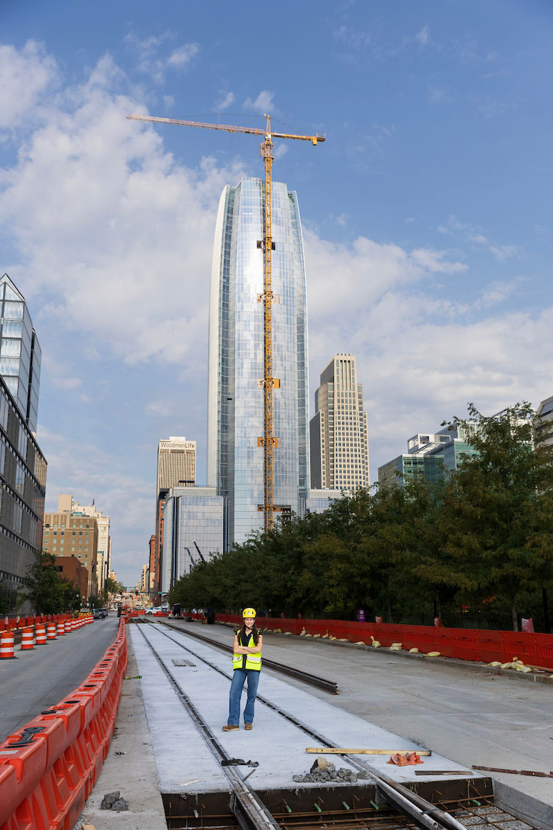 A woman in a reflective vest and a hard hat stands along the Omaha streetcar route in front of the Mutual of Omaha building.