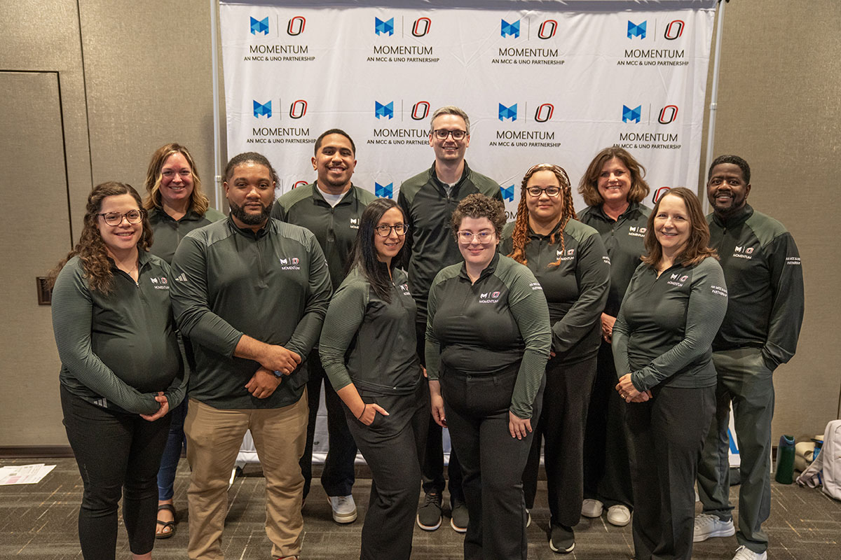 11 people in matching gray quarterzips pose in front of the Momentum backdrop.